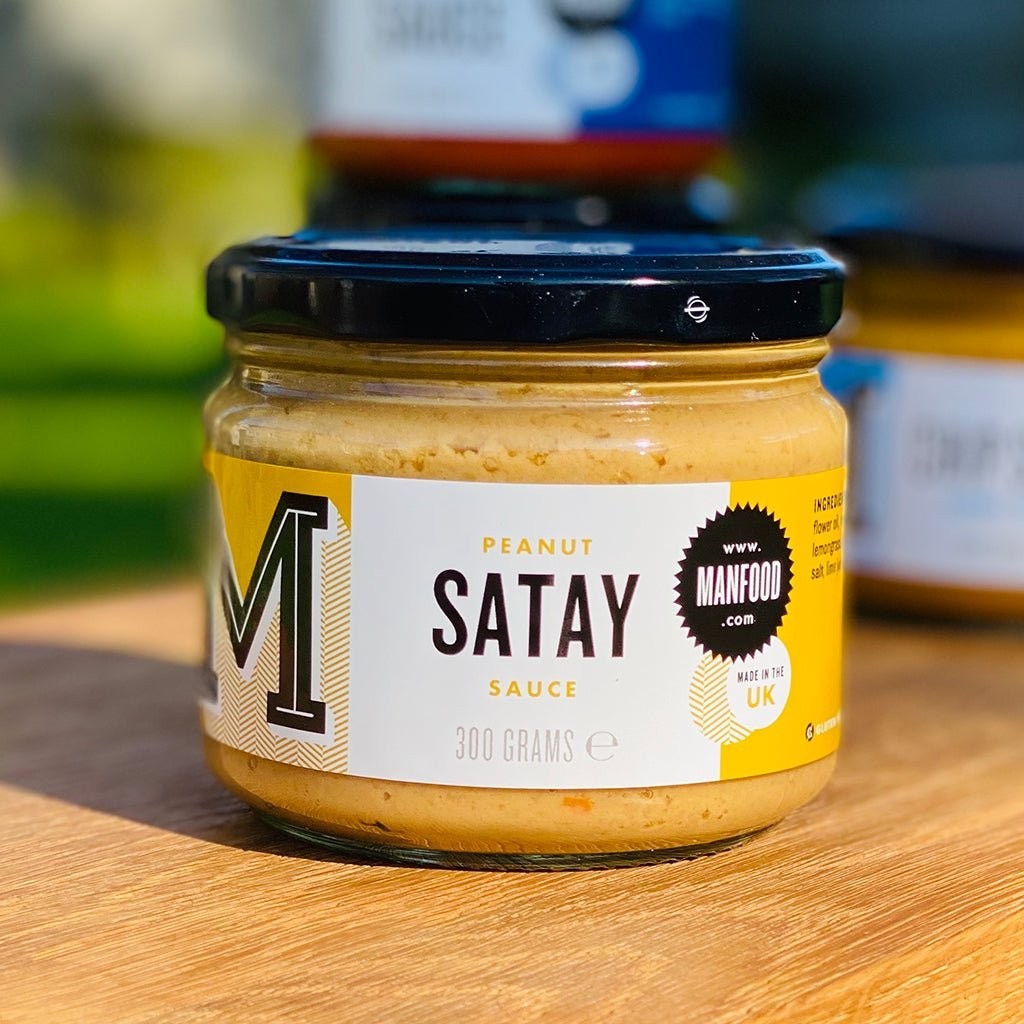 Manfood Peanut Satay Sauce in a 300g glass jar with a yellow and white label on a wooden surface.