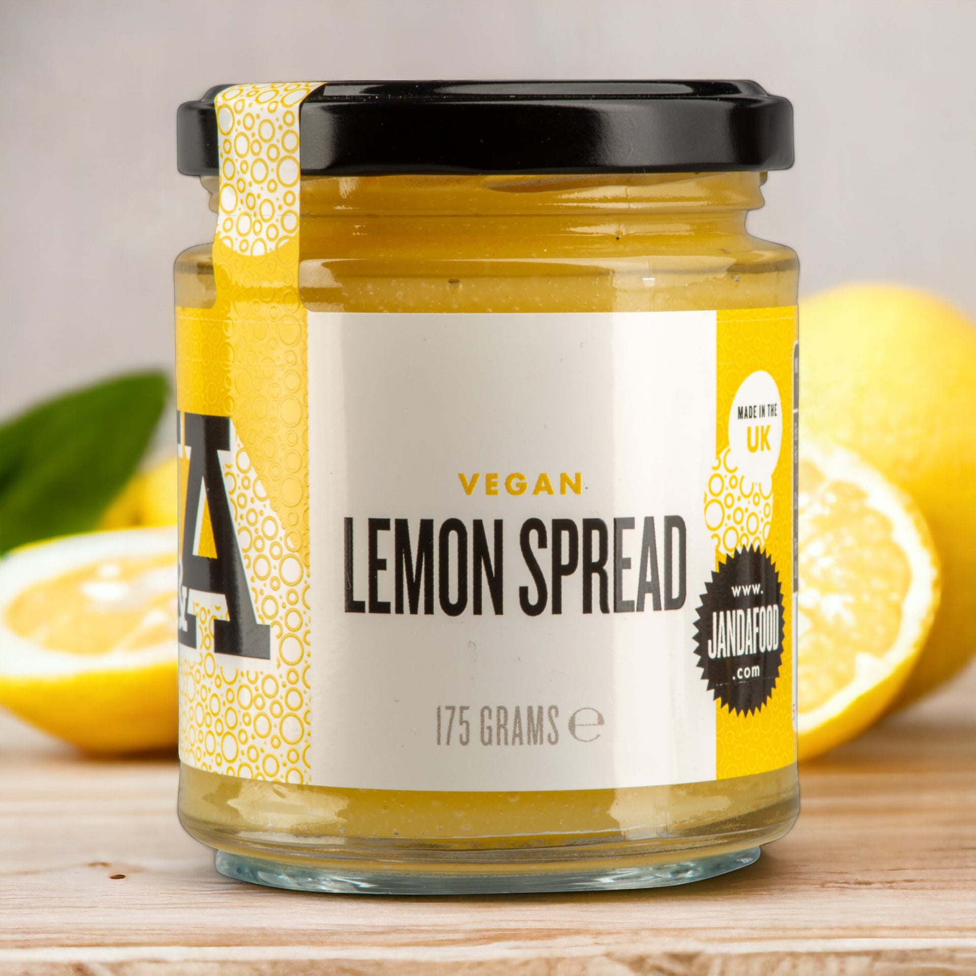 Manfood vegan lemon curd in a 175g glass jar with a yellow label, displayed with fresh lemons on a wooden table